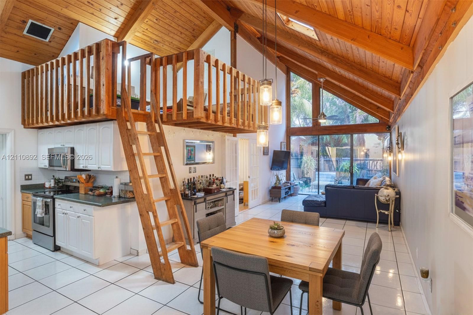 Vaulted wood-plank ceiling featuring exposed beams, mezzanine level with wooden railings, floor-to-ceiling glass paneling, tile flooring, and integrated pendant lighting Vaulted wood-plank ceiling featuring exposed beams, mezzanine level with wooden railings, floor-to-ceiling glass paneling, tile flooring, and integrated pendant lighting