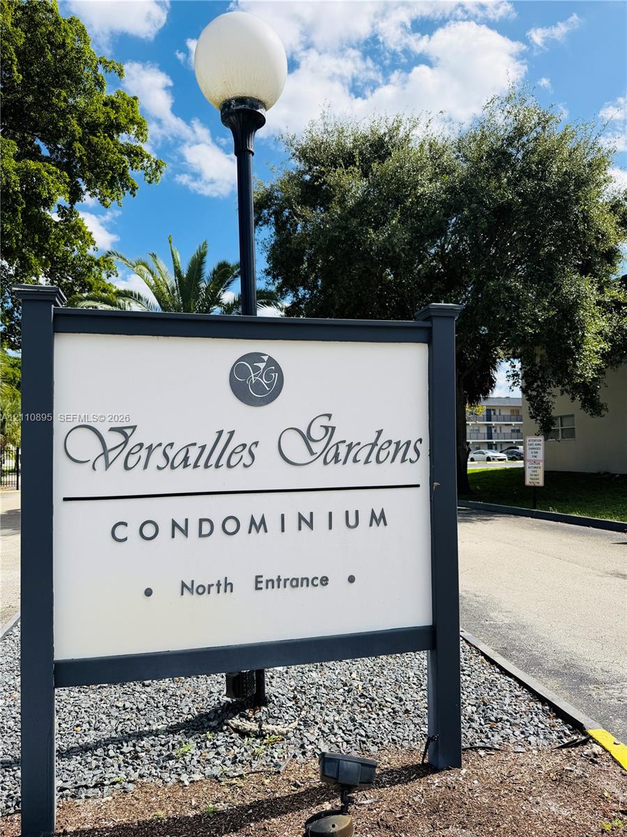 Versailles Gardens Condominium monument sign featuring a dark metal frame, spherical post-top lighting, and decorative landscaping rock bed