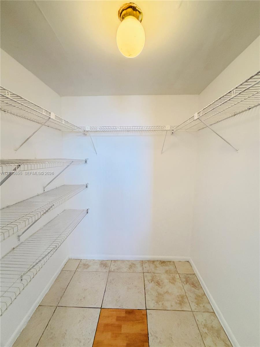 Walk-in storage space featuring white wire shelving, neutral floor tile, and a flush-mount overhead light fixture