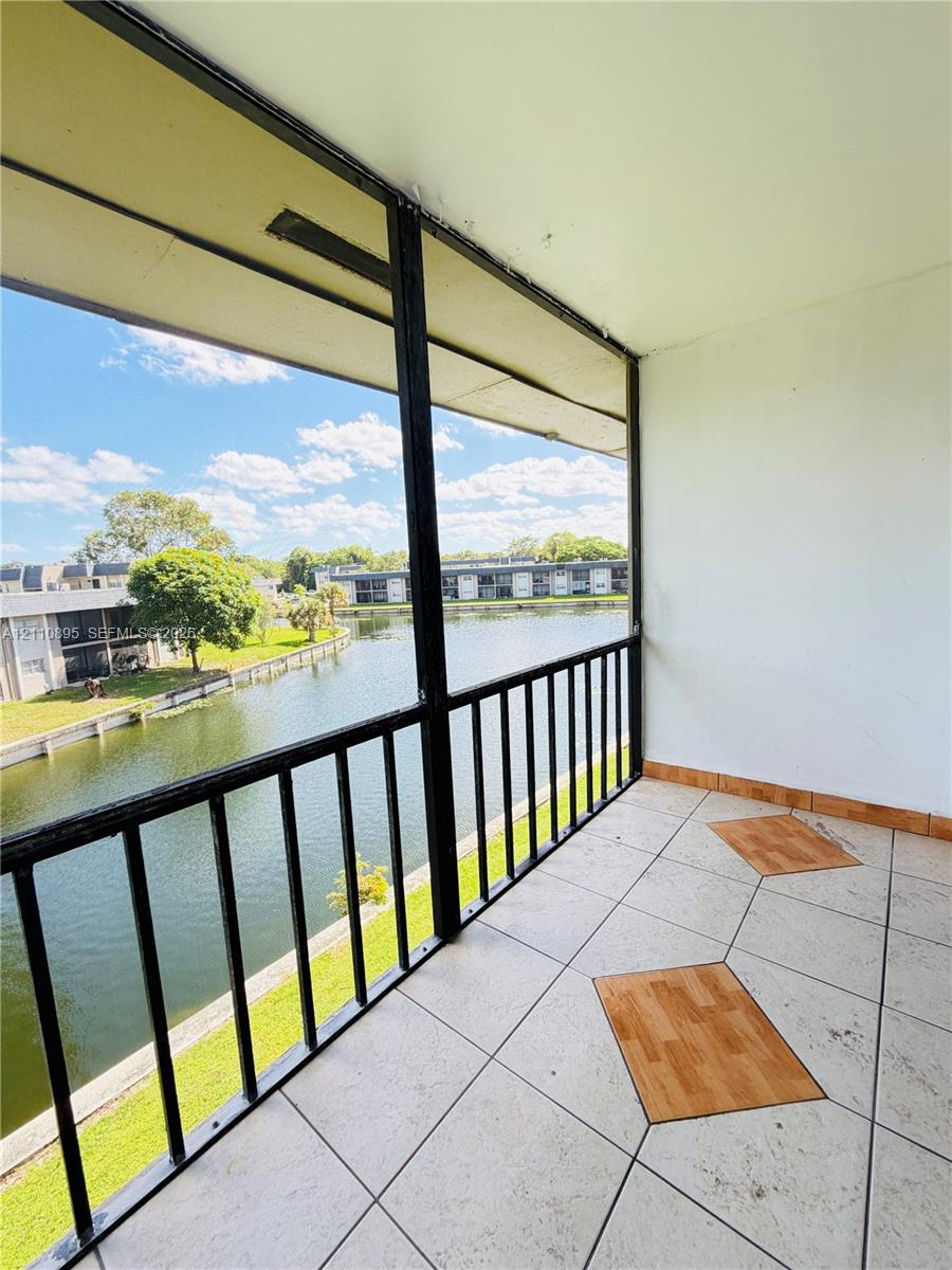Screened-in balcony featuring ceramic tile flooring with decorative inlay and a metal railing overlooking a water feature