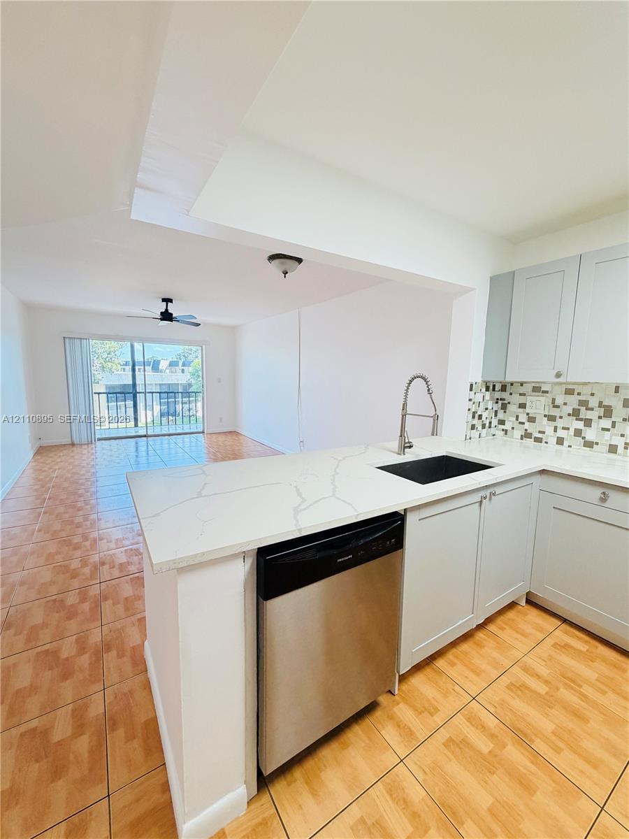 Kitchen featuring light-toned shaker cabinetry, quartz countertops with veining, a stainless steel dishwasher, a dark basin sink with a high-arch pull-down faucet, and a mosaic tile backsplash