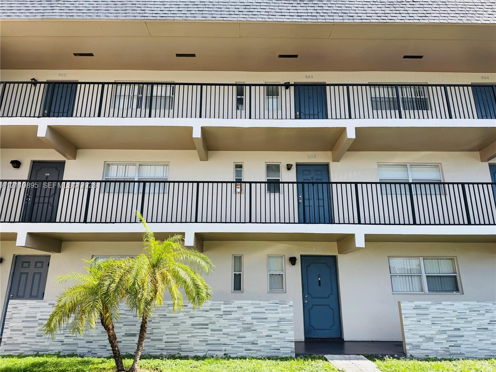 Multi-level exterior featuring stacked balconies with black metal railings, textured stone-veneer privacy walls, and neutral stucco facade