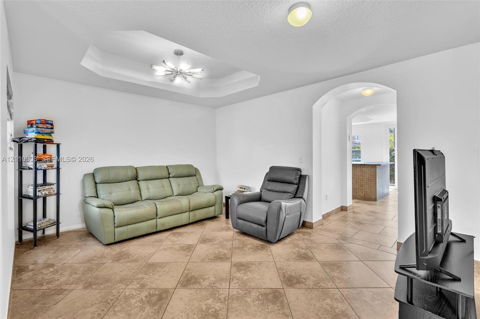 Tray ceiling with multi-arm chandelier, large-format ceramic tile flooring, and arched entryway