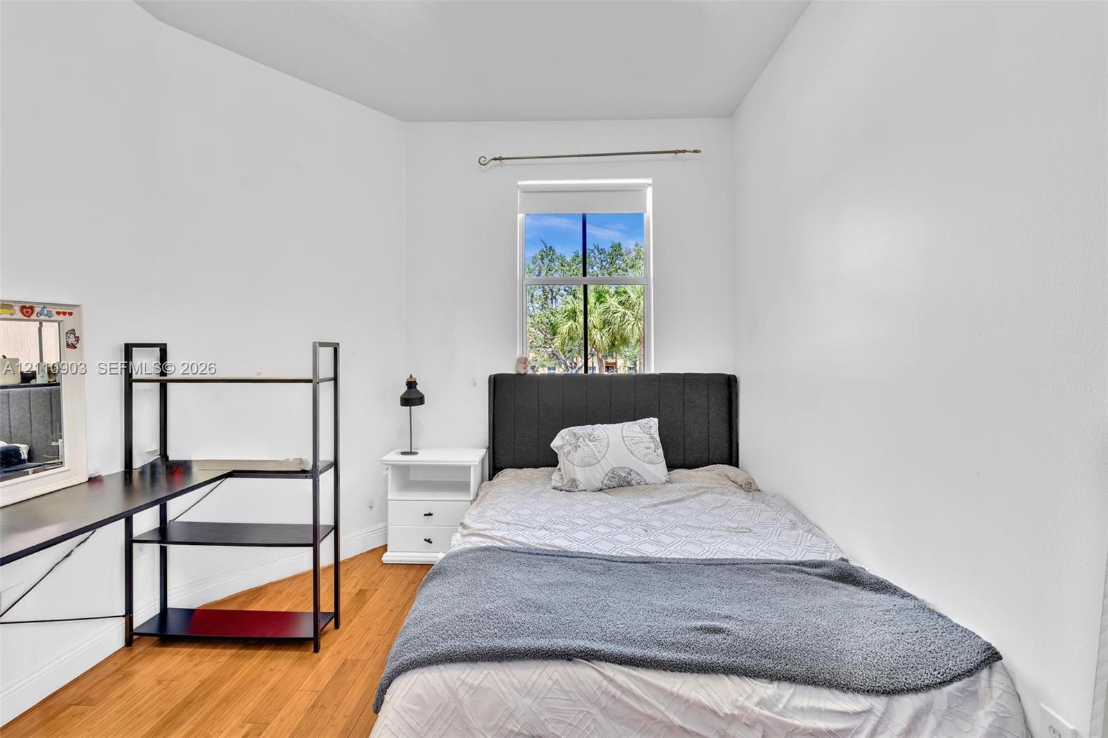Interior space featuring wood-finish flooring, white walls, and a single-hung window with a roller shade