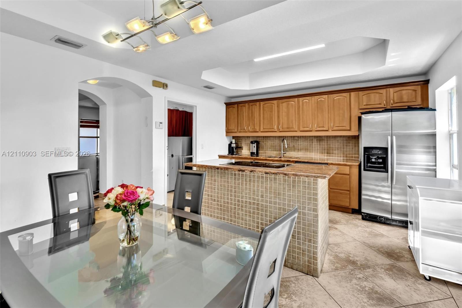 Kitchen featuring a center island with tiled exterior, stone countertops, wood cabinetry, recessed tray ceiling, and ceramic tile flooring