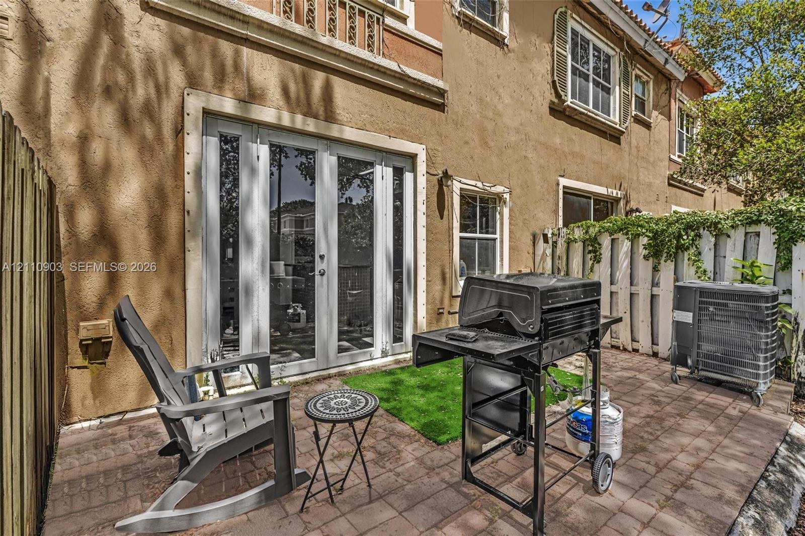 Stucco exterior featuring French glass doors, paver patio, wood-style fencing, and multi-pane windows