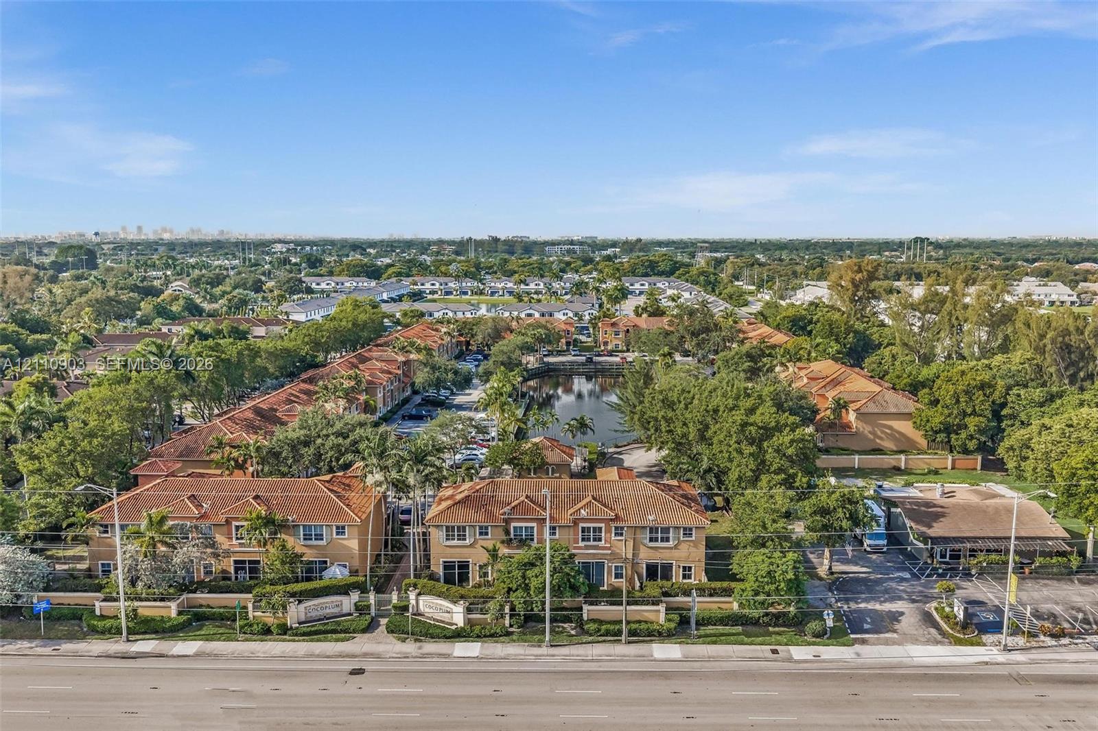 Aerial perspective of multi-family residences featuring clay tile roofing, stucco exterior finishes, gated entry, and a central water feature surrounded by mature landscaping