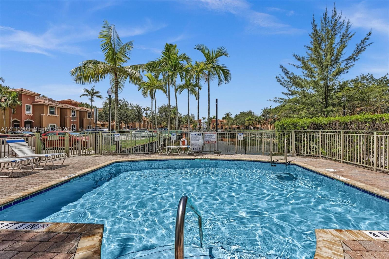Swimming pool with paver decking, metal perimeter fencing, and mature palm trees