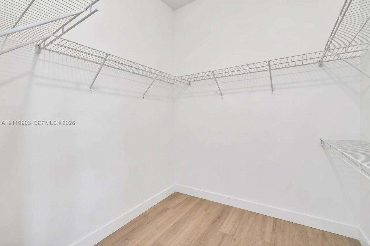 Walk-in closet featuring neutral white walls, wood-finish flooring, and multi-tier wire shelving