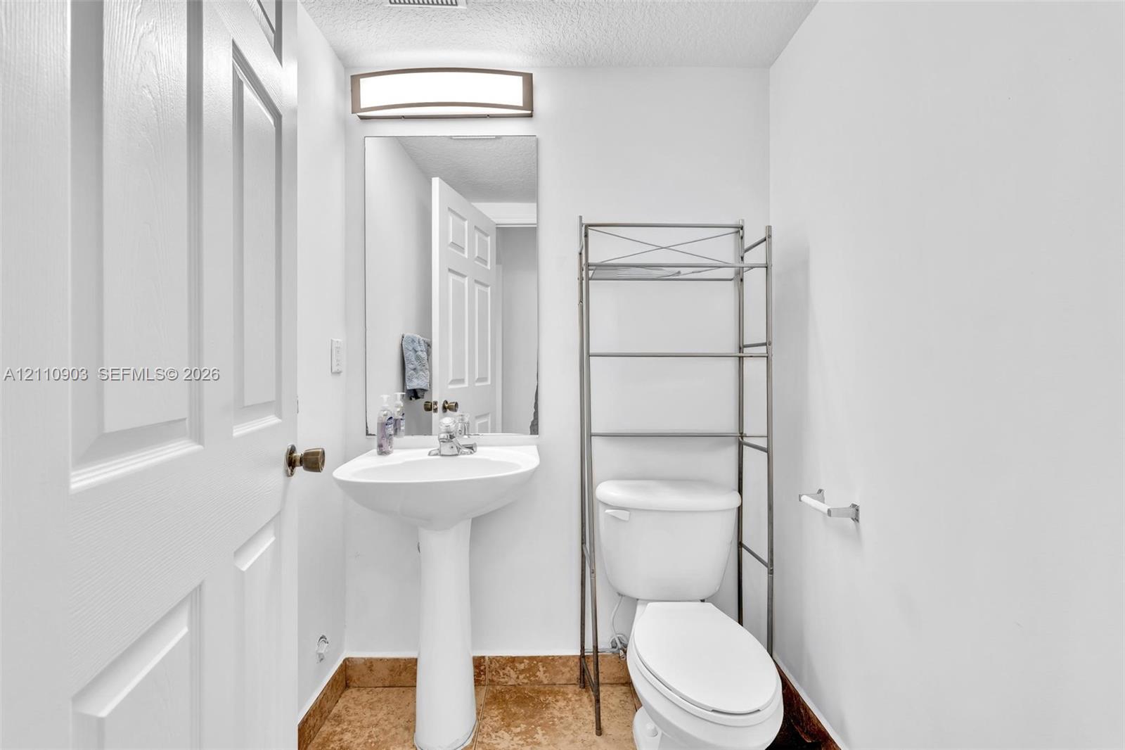 Pedestal sink with chrome faucet, framed mirror, wall-mounted light fixture, and stone-finish flooring