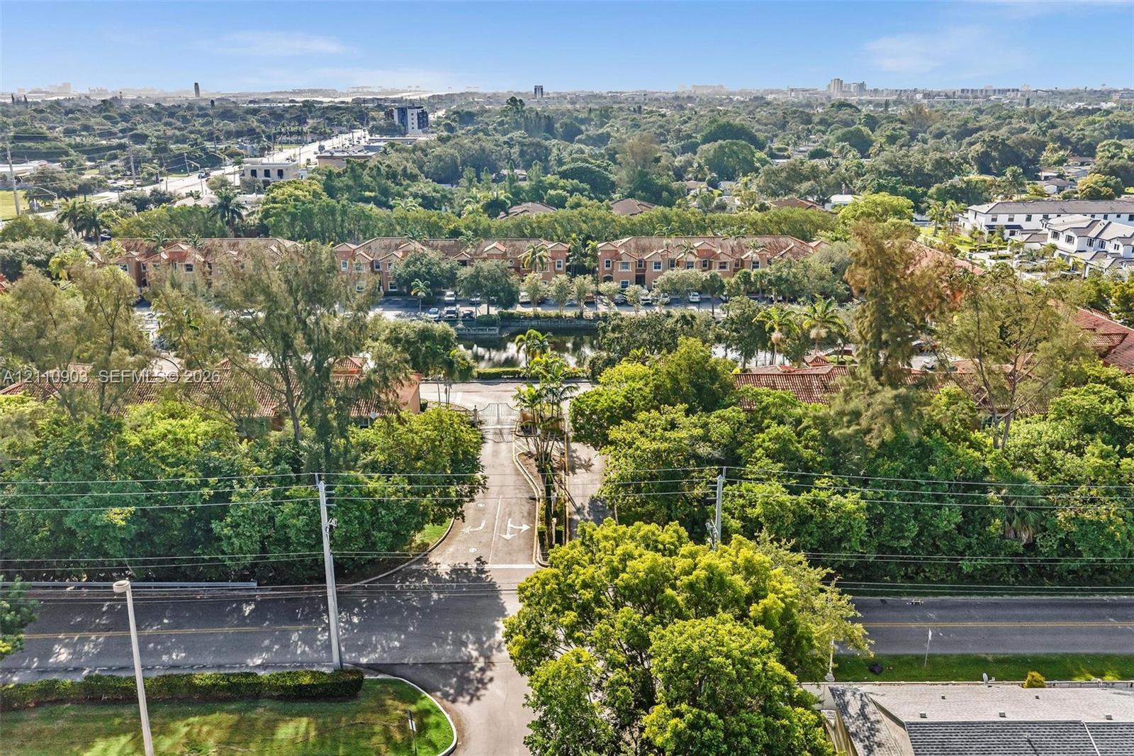 Aerial perspective of the property featuring gated site access, paved private driveways, surrounding mature canopy trees, and an onsite waterway
