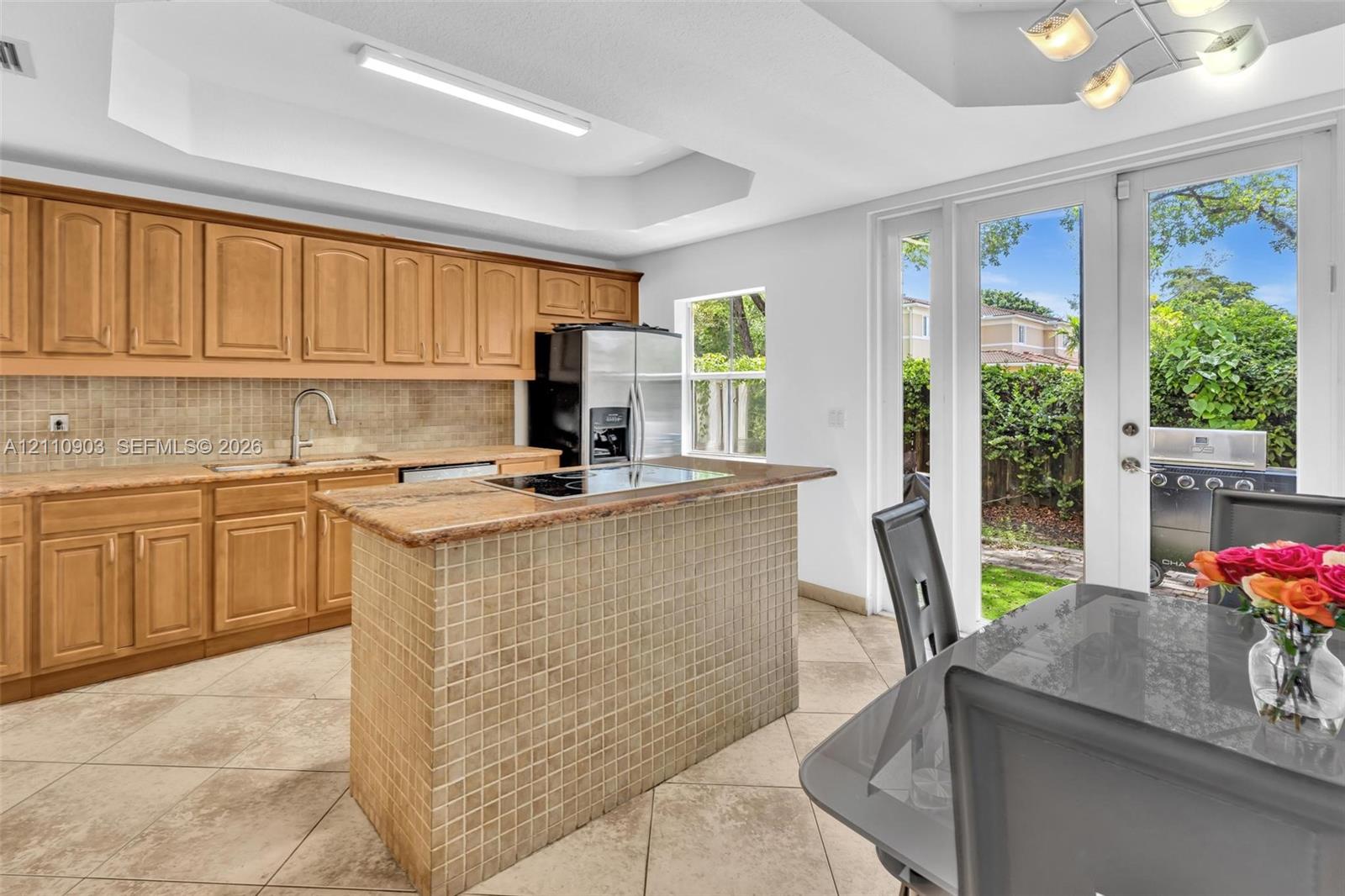 Kitchen featuring light-finish cabinetry, stone-surface counters, tile backsplash, tile-faced center island, and ceramic tile flooring