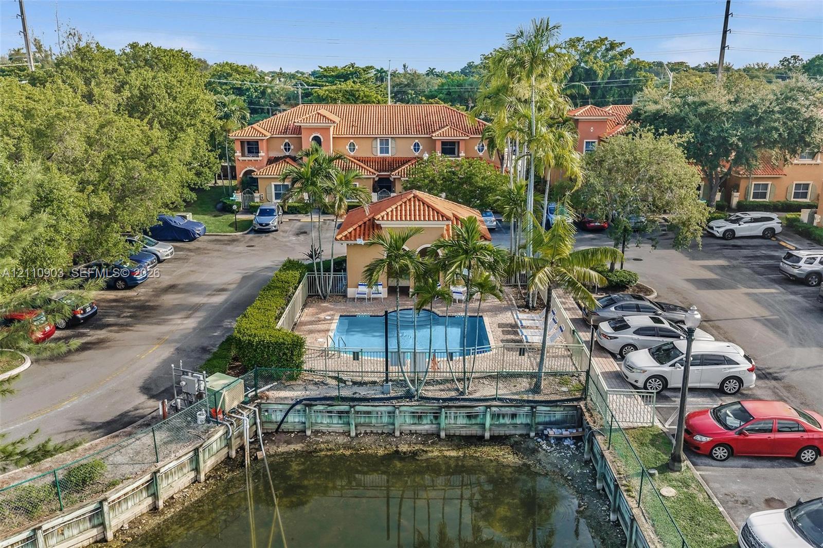 Exterior architecture featuring a tiled roof and stucco facade, communal swimming pool with a covered pavilion, and a fenced waterfront bulkhead