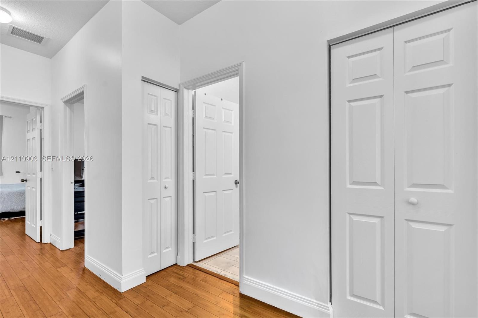 Interior hallway featuring wood-finish flooring, white walls, and multiple bi-fold closet doors