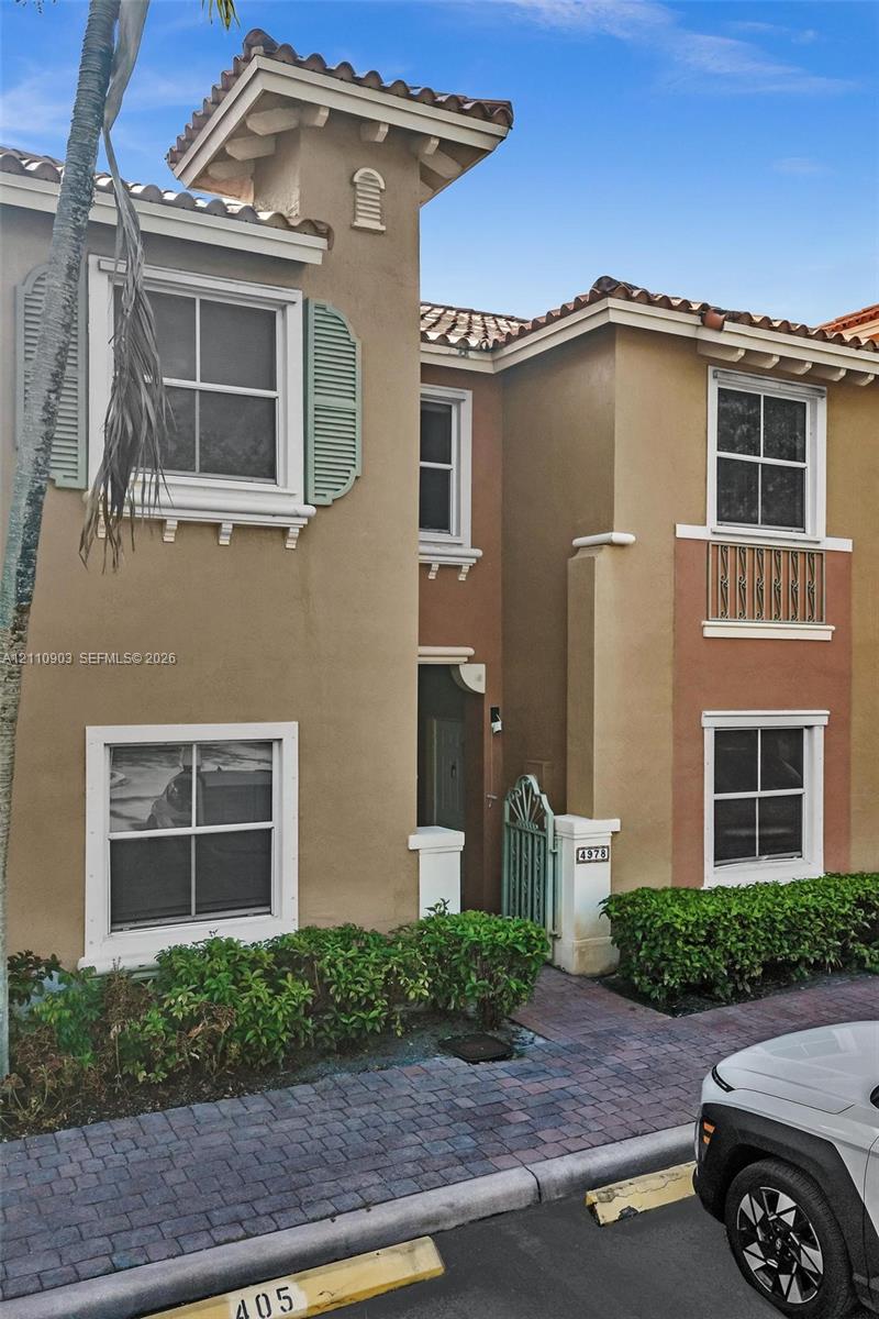 Stucco exterior featuring tile roof accents, decorative shutters, a wrought-iron gate, and a paver stone walkway
