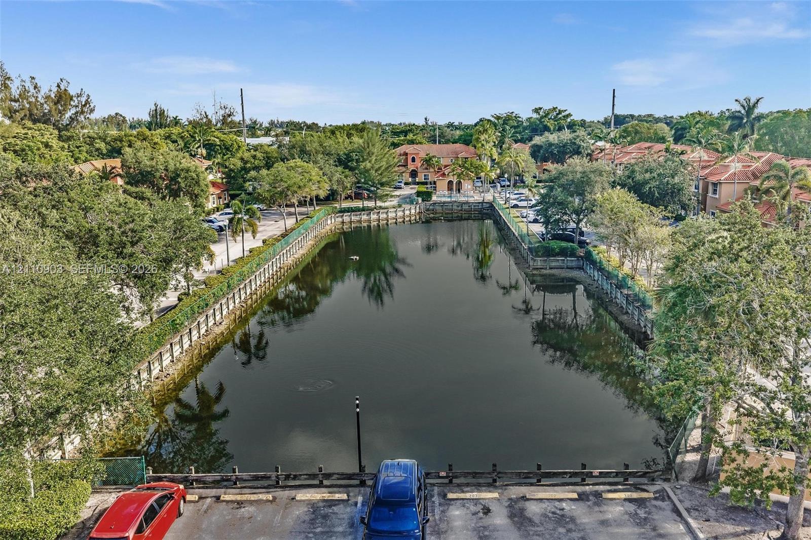 Aerial perspective of a central retention pond featuring stone-block reinforced banks, perimeter fencing, and mature trees