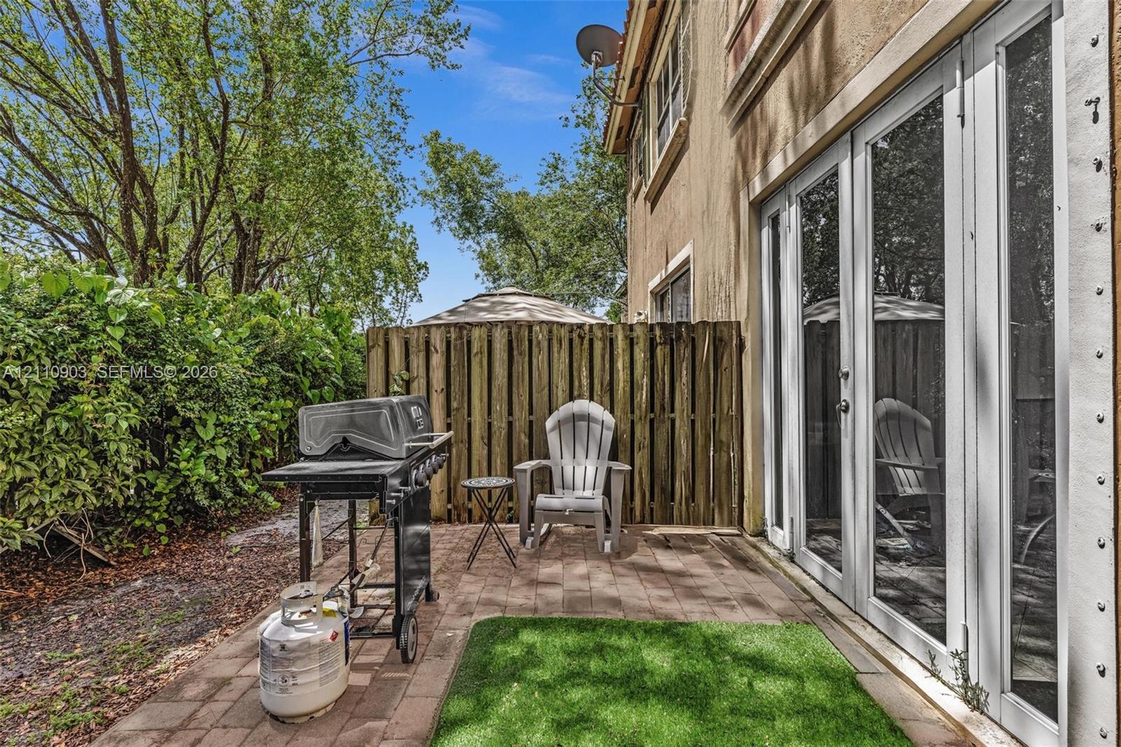 Paved patio featuring stone-finish pavers, synthetic turf inlay, and white-framed multi-panel glass doors