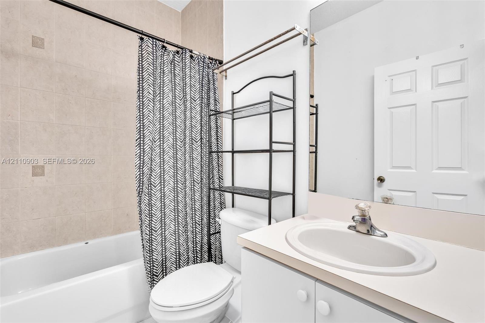 Bathroom featuring a tub-shower combination with floor-to-ceiling beige tile surround, vanity with an integrated oval sink, and a large frameless wall-mounted mirror
