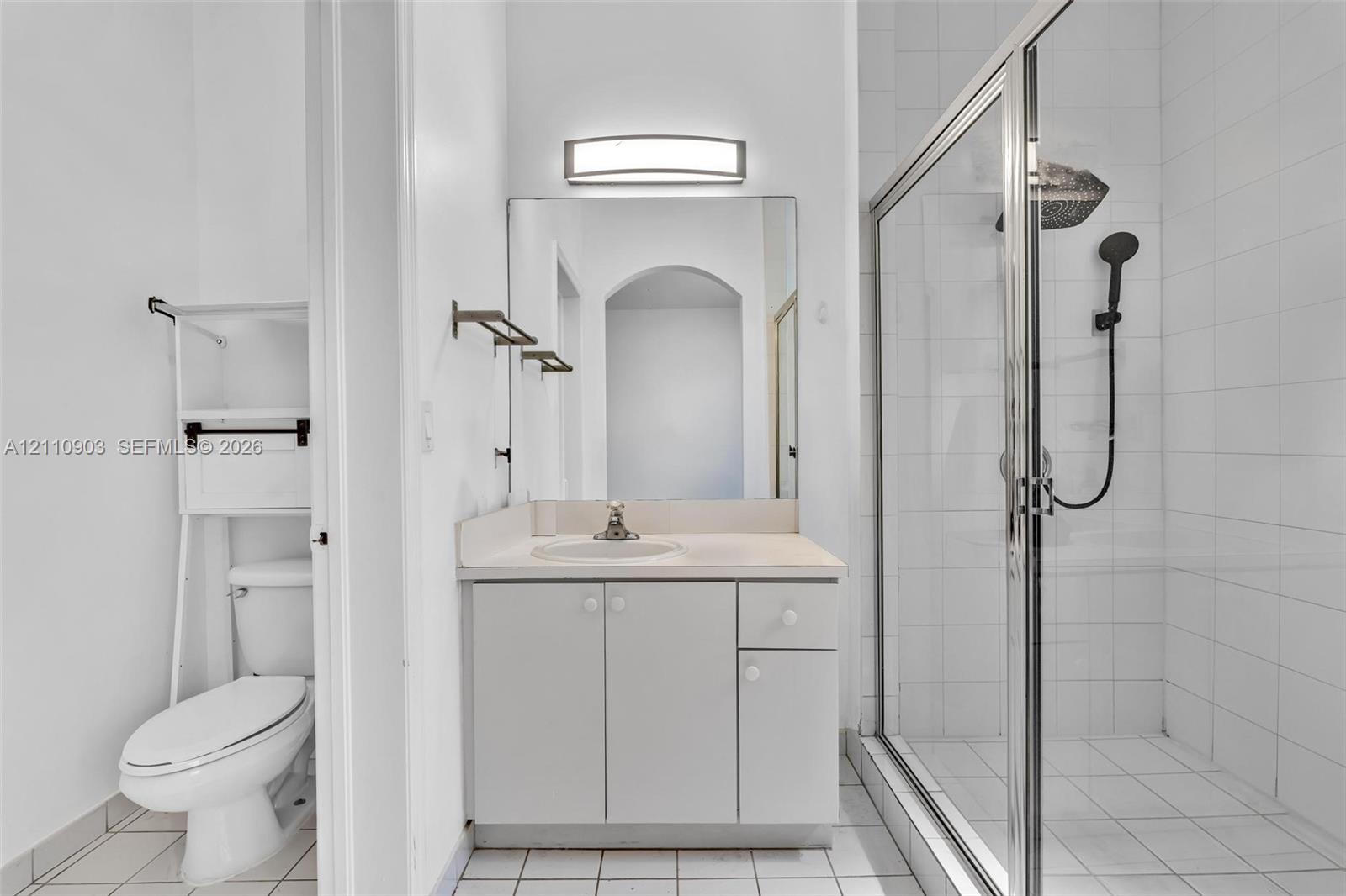 Bathroom featuring a vanity with integrated sink, rectangular wall-mounted light fixture, and a glass-enclosed shower with a handheld showerhead and wall-mounted tile surround