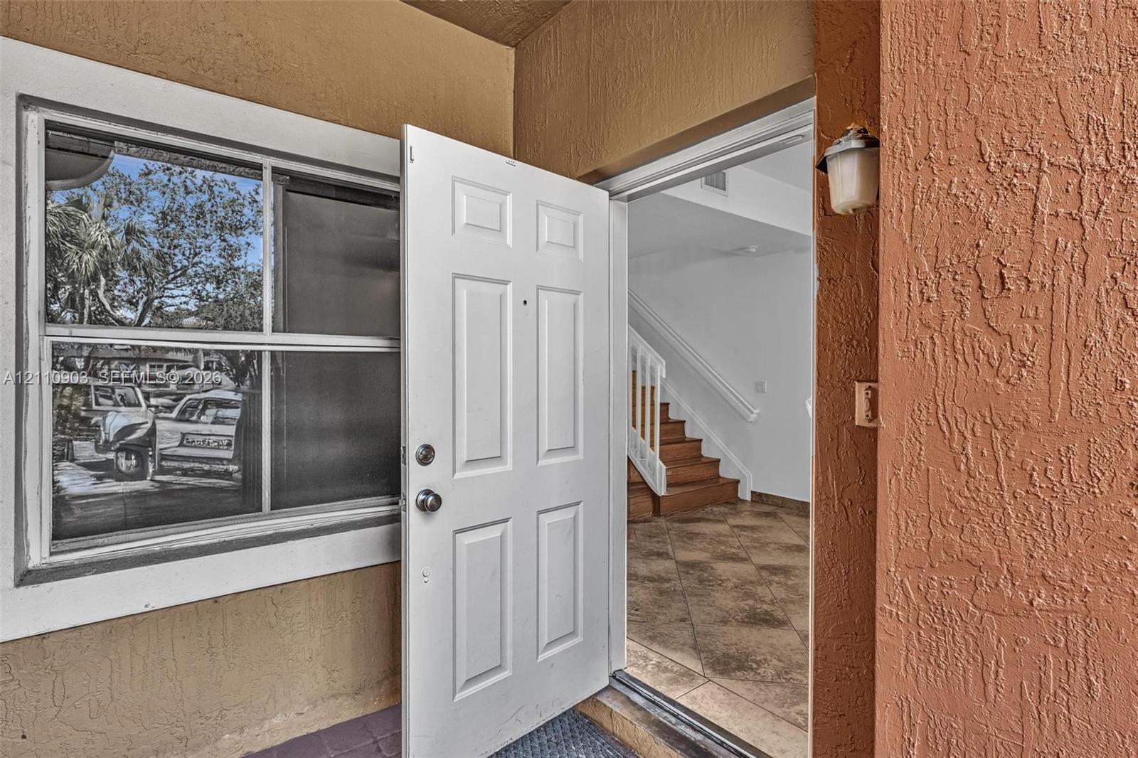 Stucco exterior entryway featuring a multi-panel front door, decorative wall-mounted lighting, and a single-hung window with a light-colored frame