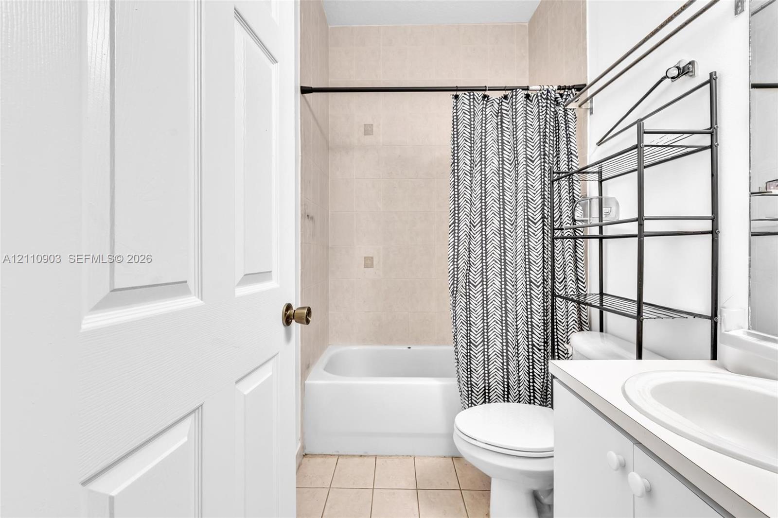 Bathroom featuring a porcelain tub with tile surround, tile flooring, and a white vanity with an integrated basin