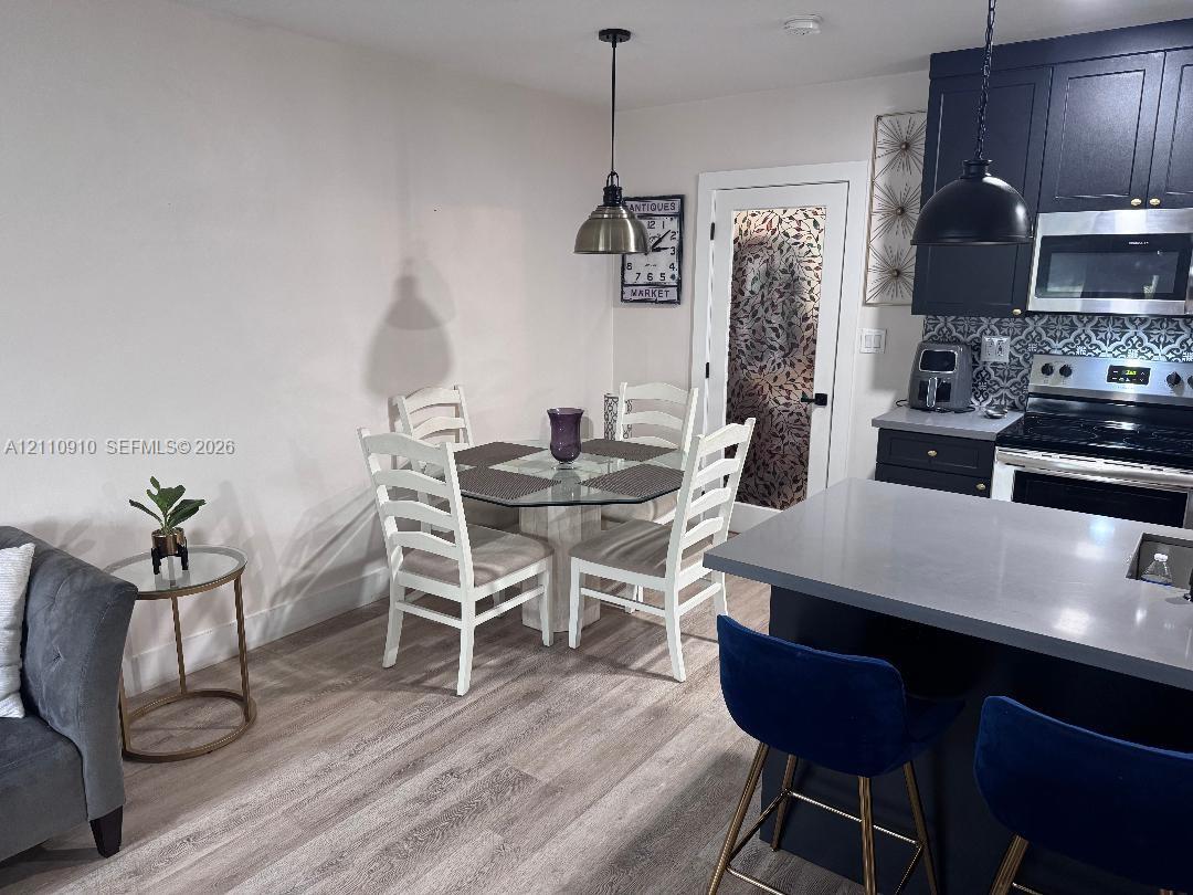 Kitchen featuring dark cabinetry, solid-surface countertops, decorative backsplash, wood-finish flooring, and dual hanging pendant lights
