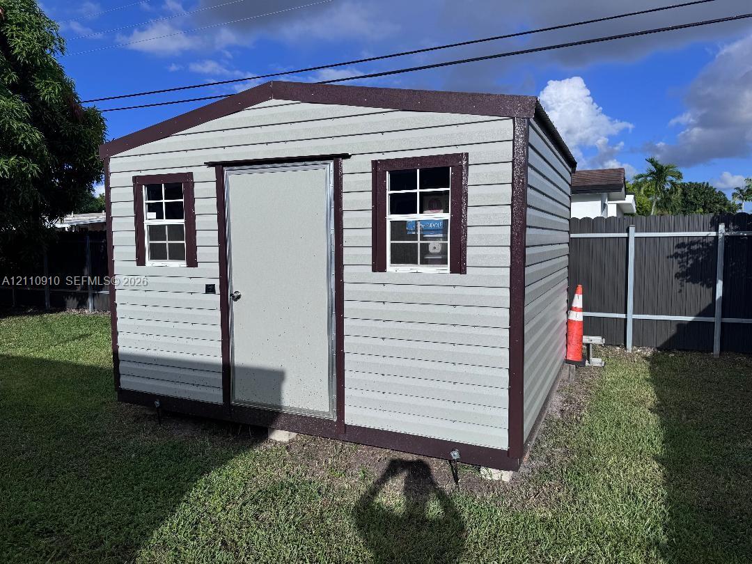 Detached exterior storage structure featuring horizontal siding, dark trim, two grid-patterned windows, and a secure entry door