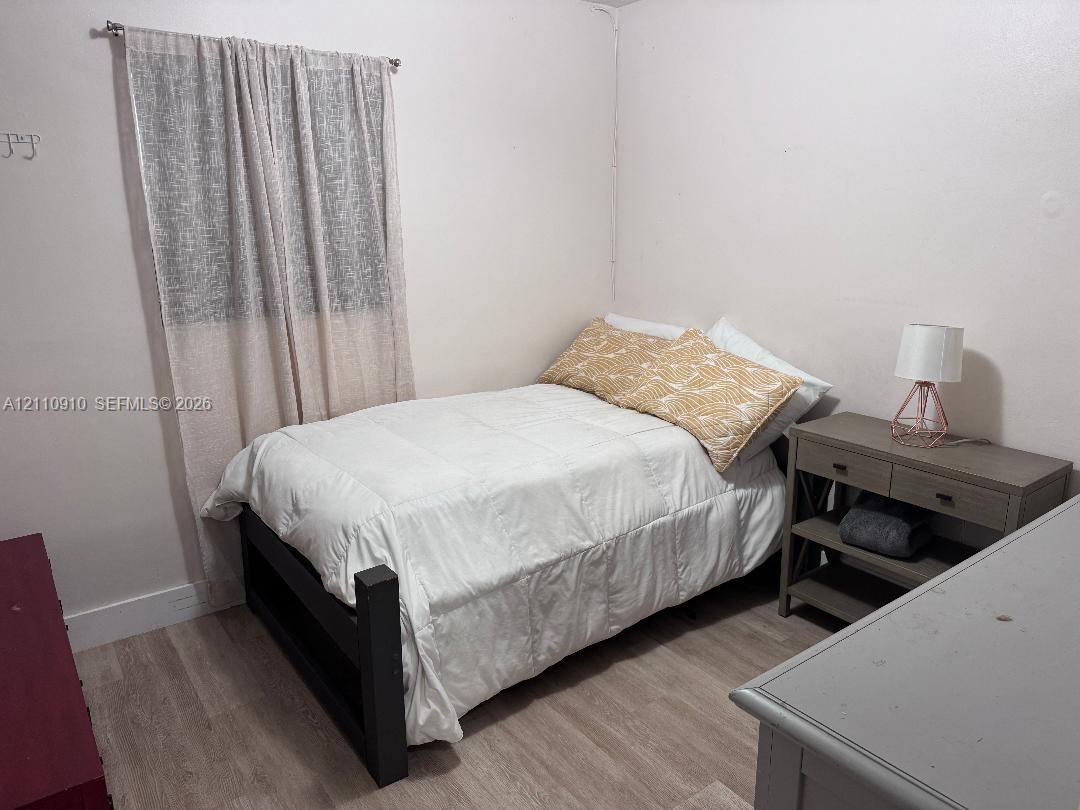 Neutral-toned room featuring wood-finish flooring and a single-window configuration with an installed curtain rod