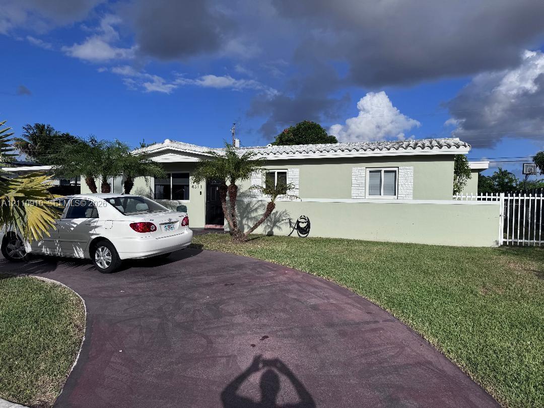 Single-story residence featuring a tile roof, light-colored exterior finish, masonry perimeter wall, white metal fencing, and a curved paved driveway