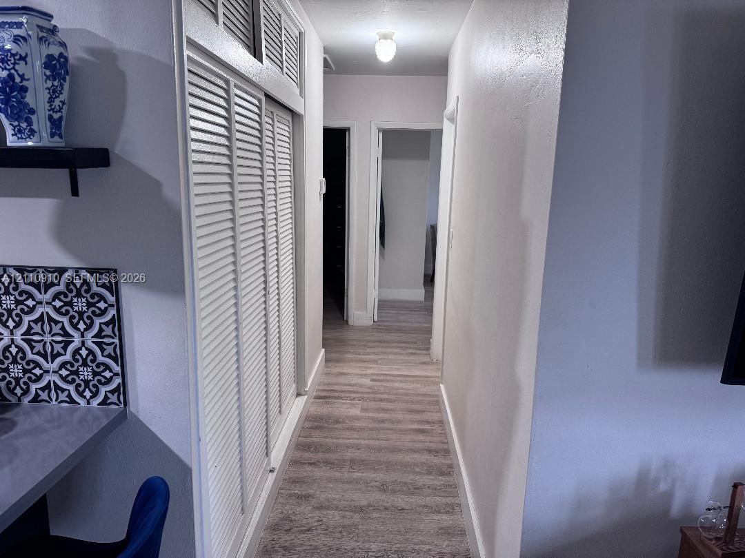 Hallway featuring wood-finish flooring, floor-to-ceiling bi-fold louvered doors, and overhead lighting