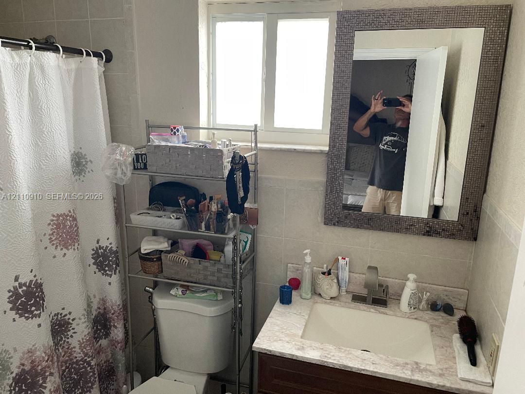 Bathroom featuring a single-sink vanity with a stone-composite countertop, integrated rectangular basin, tiled wall surround, and a framed wall-mounted mirror