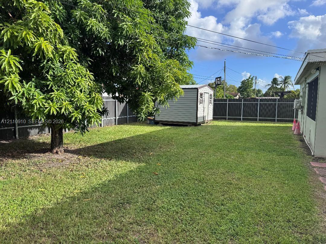 Backyard featuring a grass lawn, mature tree, standalone storage shed, and full-perimeter privacy fencing