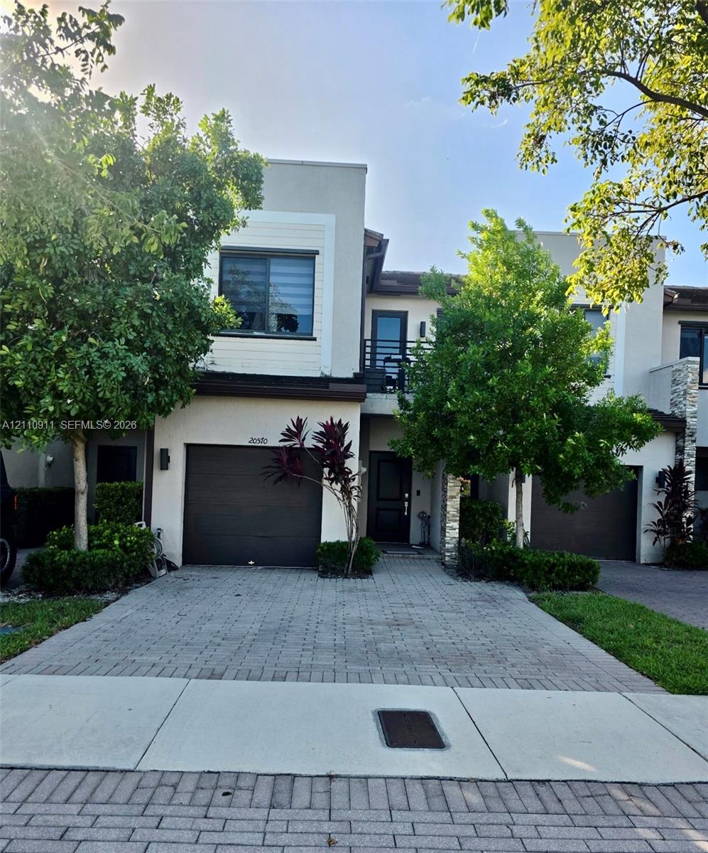 Contemporary exterior featuring stucco siding, stone veneer accents, a paved driveway, and an attached garage Contemporary exterior featuring stucco siding, stone veneer accents, a paved driveway, and an attached garage
