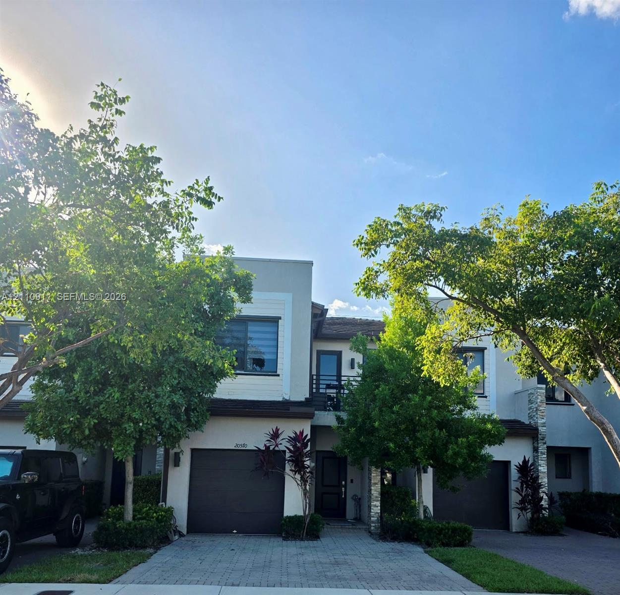 Contemporary multi-level exterior featuring light-toned smooth stucco, stone veneer accents, multi-car garages, and an upper-level balcony with metal railing
