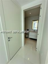 Solid-core white interior door with a contemporary metallic handle, polished tile flooring, wall-mounted floating vanity with integrated basin, and illuminated wall mirror