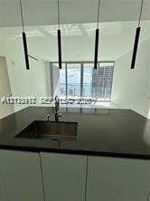 Modern kitchen island featuring a solid-surface countertop, integrated stainless steel undermount sink, gooseneck faucet, and four cylindrical pendant lights