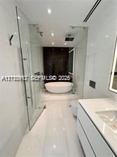 Freestanding soaking tub, glass-enclosed shower, wall-mounted vanity with integrated sink, and polished large-format tile flooring