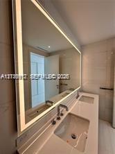 Dual-sink vanity featuring a solid surface countertop, undermount basins, polished chrome fixtures, and a large, full-width LED-backlit mirror