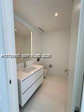 Wall-mounted white vanity with a rectangular integrated sink, stone countertop, large-format tile flooring, and a full-height backlit mirror