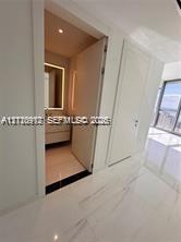 Large-format tile flooring, flush-mounted interior doors, and recessed ceiling lighting, with entry to a bathroom featuring a floating vanity and an integrated illuminated mirror