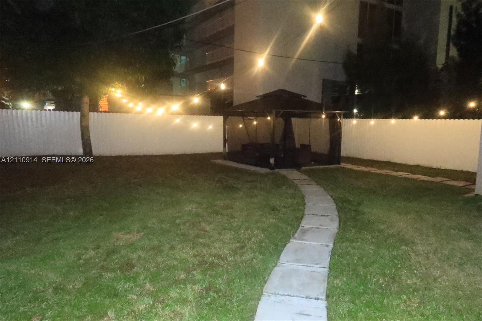 Backyard featuring a paved stone walkway, permanent gazebo structure, and perimeter white privacy fencing