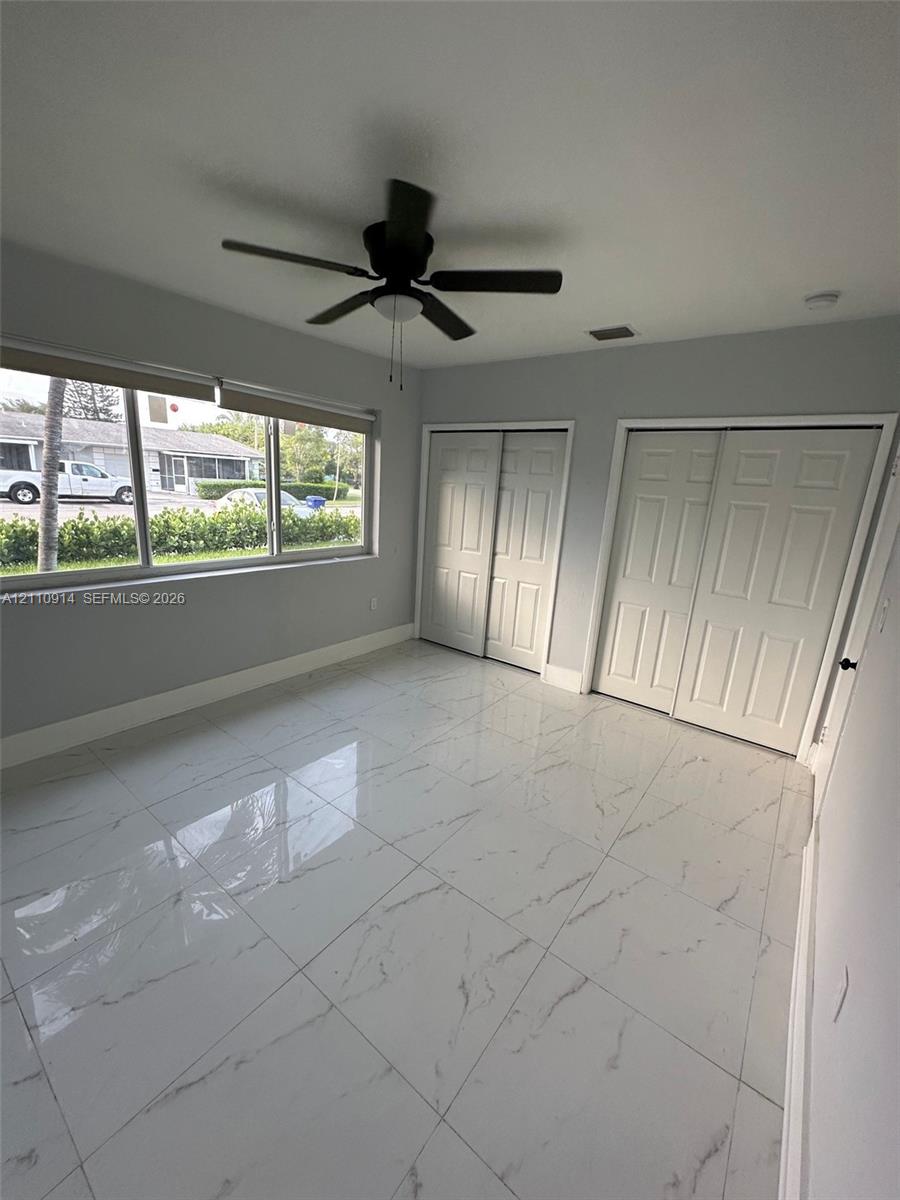 Large-format tile flooring with veining detail, multi-panel sliding closet doors, and a ceiling fan with integrated lighting