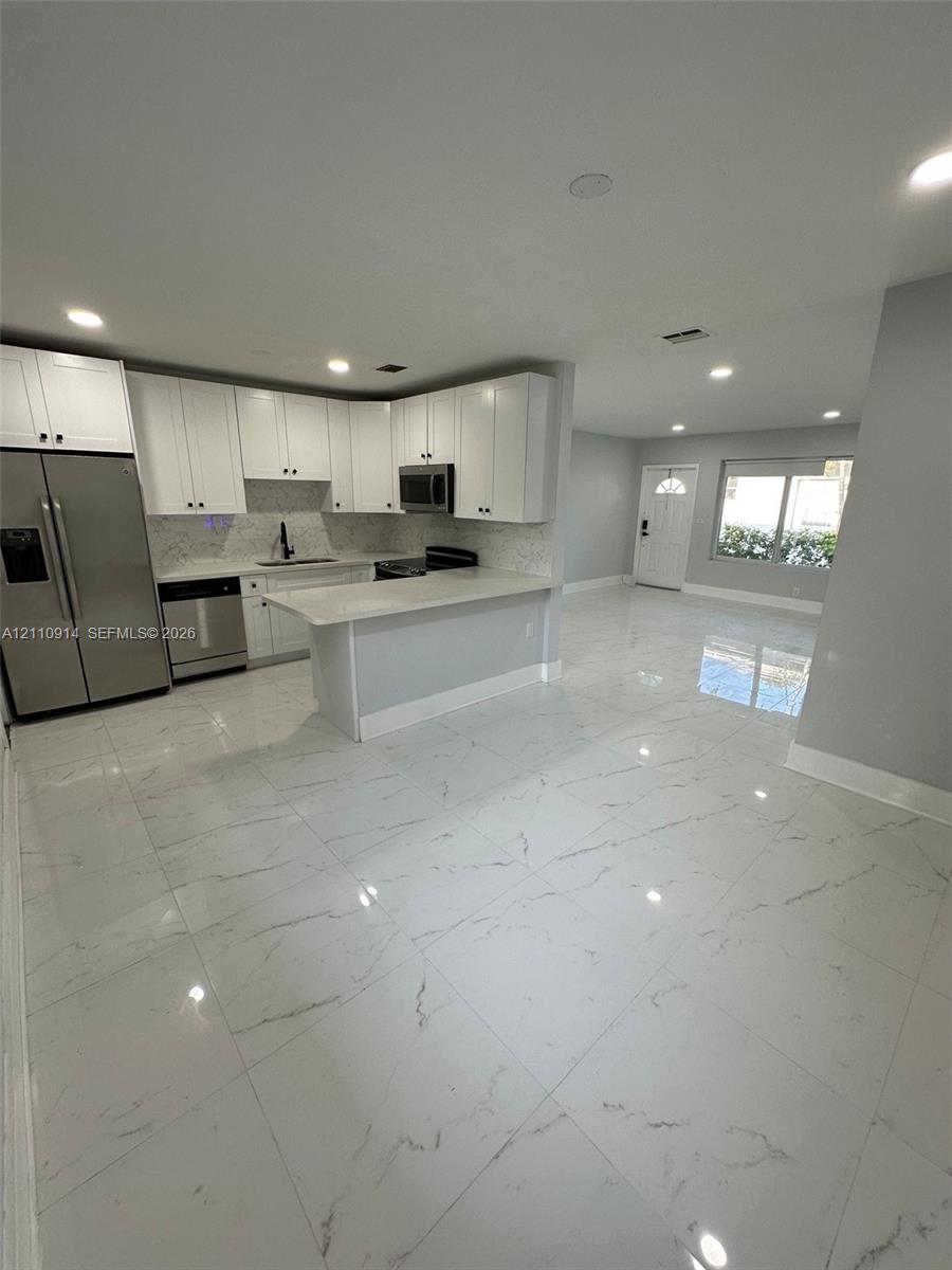 Kitchen featuring white shaker-style cabinetry, quartz countertops, a peninsula with bar seating, stainless steel appliances, and large-format porcelain tile flooring