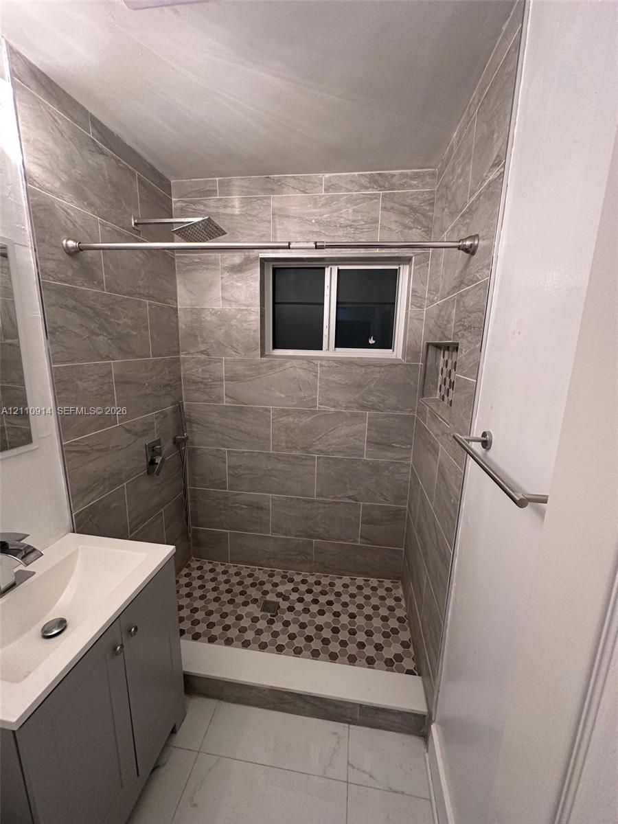 Bathroom featuring a shower with large-format stone-patterned tile, hexagonal floor tile, built-in tiled niche, rainfall showerhead, and gray vanity cabinet