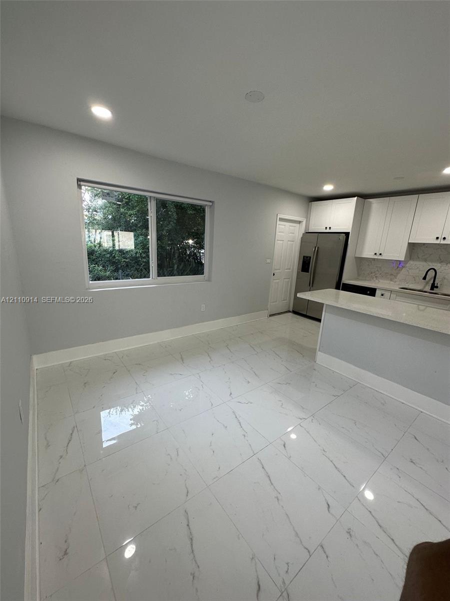 Large-format tile flooring with a neutral-veined finish, white shaker-style cabinetry, quartz countertops, and recessed lighting