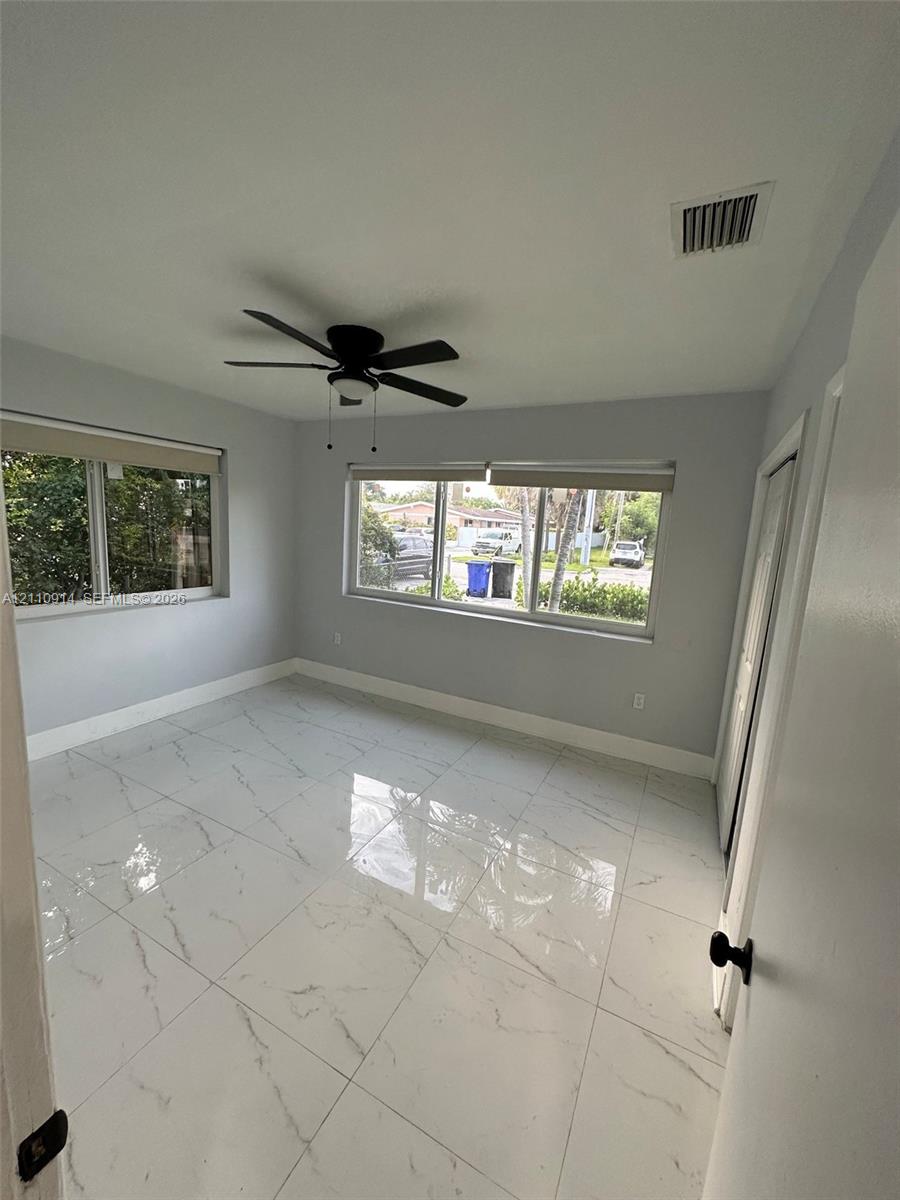 Large-format, polished stone-finish floor tiling featuring grey veining, ceiling fan with integrated lighting, and multiple windows with roller shades