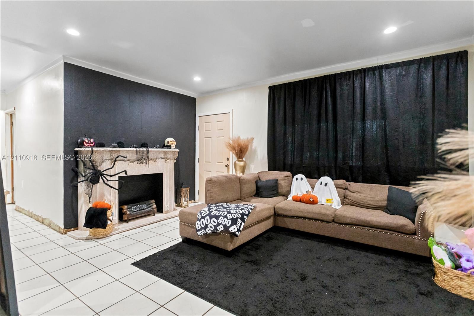 Living area featuring neutral tile flooring, a fireplace with a decorative stone-finish mantle, recessed ceiling lighting, and a prominent black accent wall