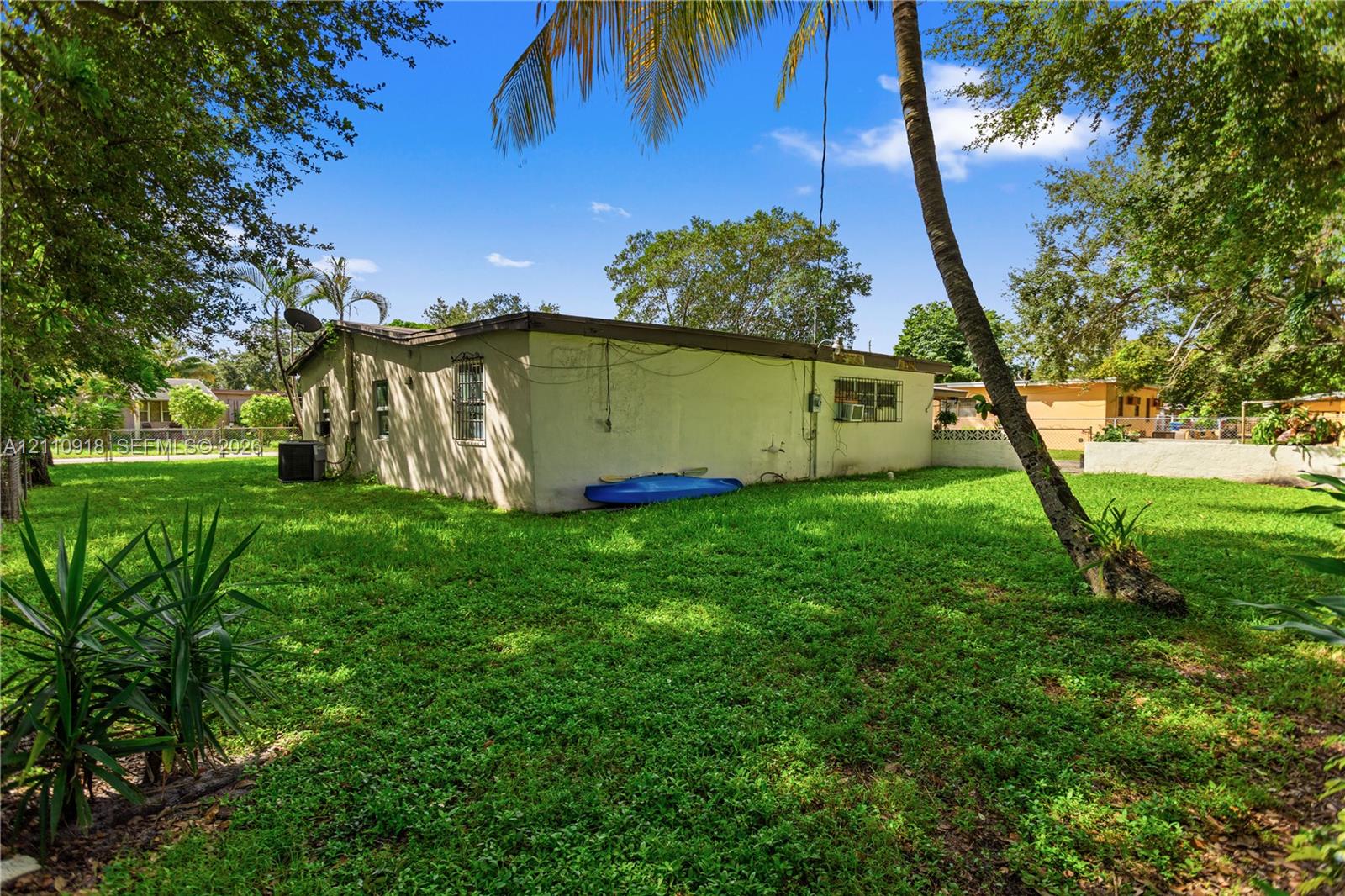 Stucco exterior featuring mature landscaping, palm trees, and an expansive grass lawn