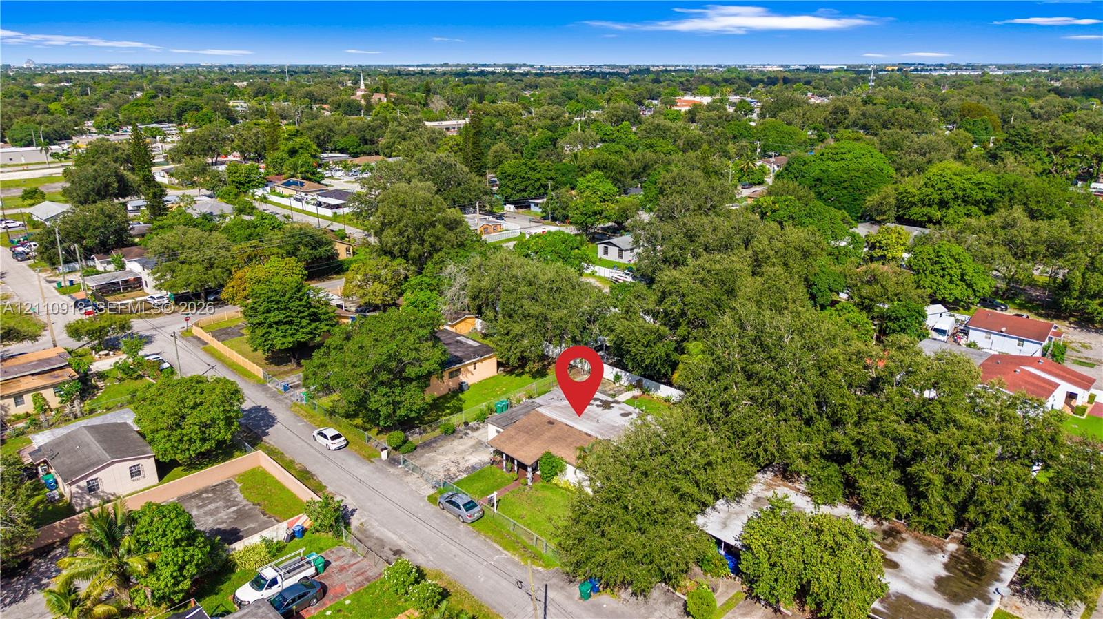Aerial perspective of property featuring a shingled roof, paved driveway, and established tree canopy