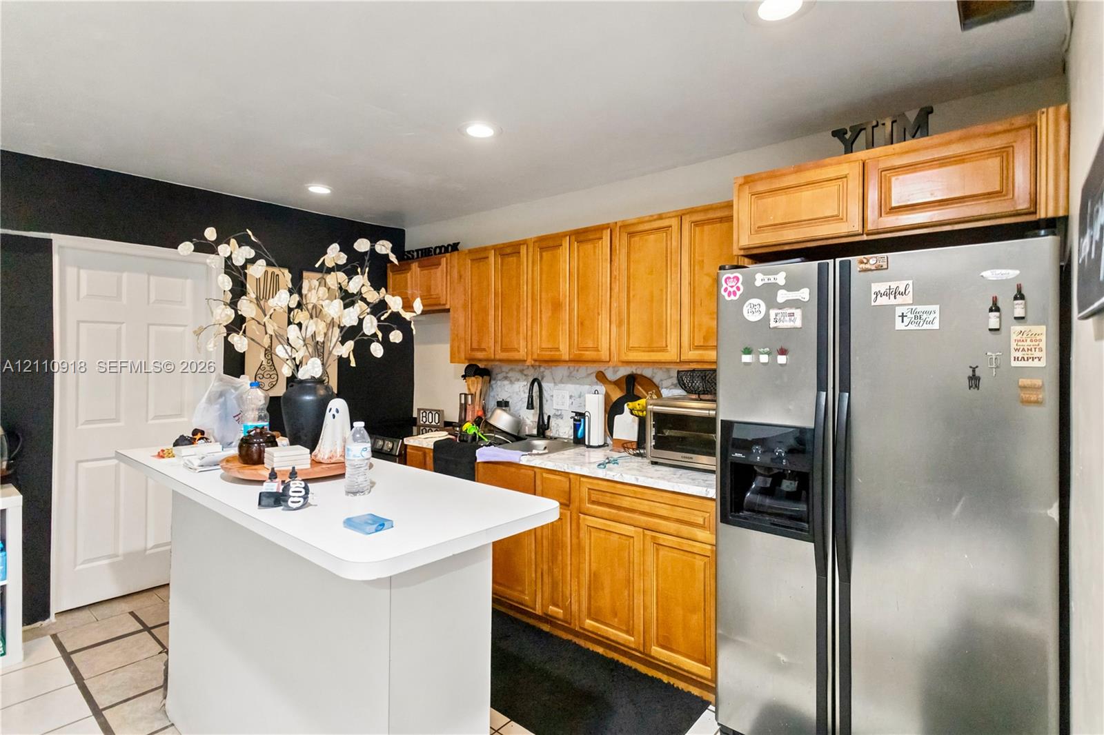 Kitchen featuring natural wood cabinetry, white countertops, recessed lighting, and a stainless steel refrigerator